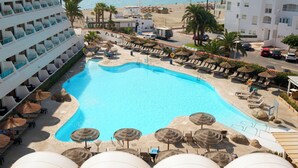 A pool area with lounge chairs and umbrellas, a view of the beach, and a building with balconies. - Alua Golf Trinidad (Roquetas de Mar)