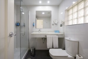 A modern bathroom with a glass shower enclosure, a white sink with a mirror above, and a toilet. - Alua Golf Trinidad (Roquetas de Mar)