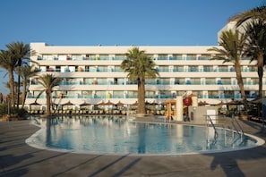Un hôtel doté d’une piscine, de palmiers et d’un immeuble à plusieurs étages avec des balcons.