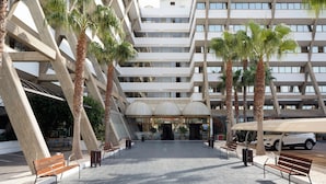 A modern building with a unique angular design, featuring multiple floors and a central atrium with a glass ceiling. - Alua Golf Trinidad (Roquetas de Mar)