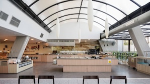 A modern restaurant with a central island, seating area, and a high ceiling with skylights. - Alua Golf Trinidad (Roquetas de Mar)