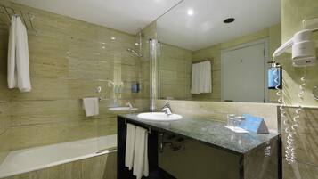 Un baño moderno con ducha envuelta en vidrio, un lavamanos con espejo y un secador de pelo sobre un soporte.