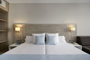 A double bed with two pillows, bedside lamps, a nightstand with a phone, and a grey armchair.