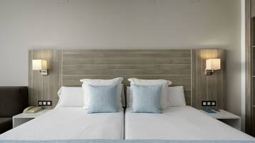 Una habitación de hotel con una cama doble, dos lámparas de noche, una mesita de noche con un teléfono y una pequeña mesa con un libro y un control remoto.