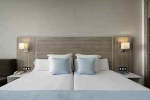 A hotel room with a double bed, two bedside lamps, a nightstand with a phone, and a small table with a book and a remote. - Alua Golf Trinidad (Roquetas de Mar)