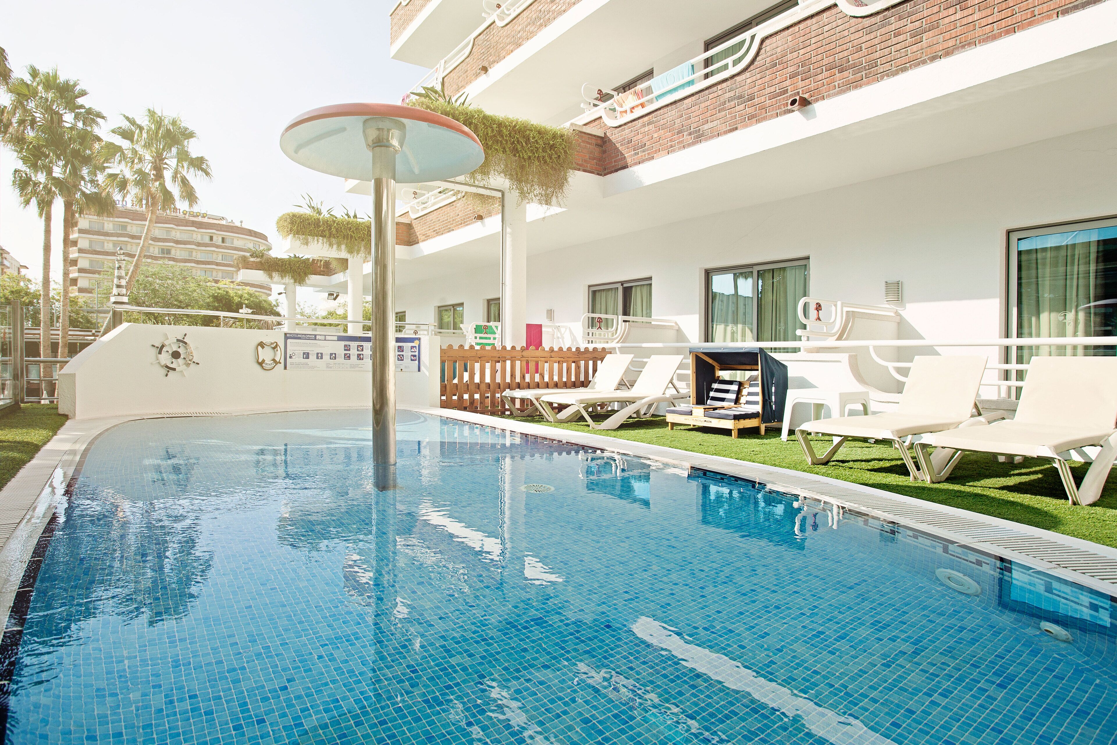 Una piscina con sillas de descanso y un toldo, rodeada por un edificio blanco con balcones.