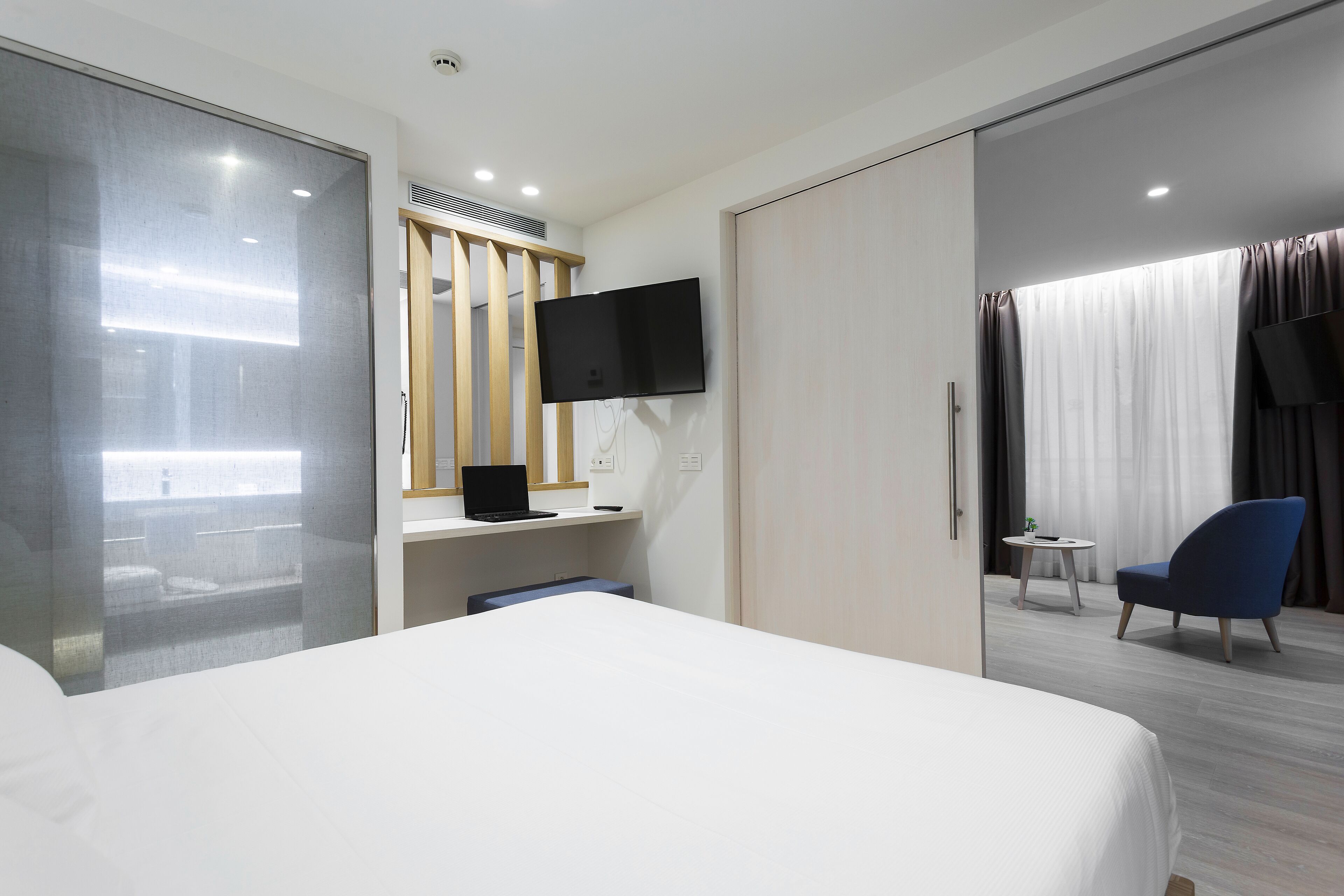 Habitación de hotel con cama, escritorio con ordenador portátil, televisor montado en la pared, silla y vistas a la ciudad desde la ventana.