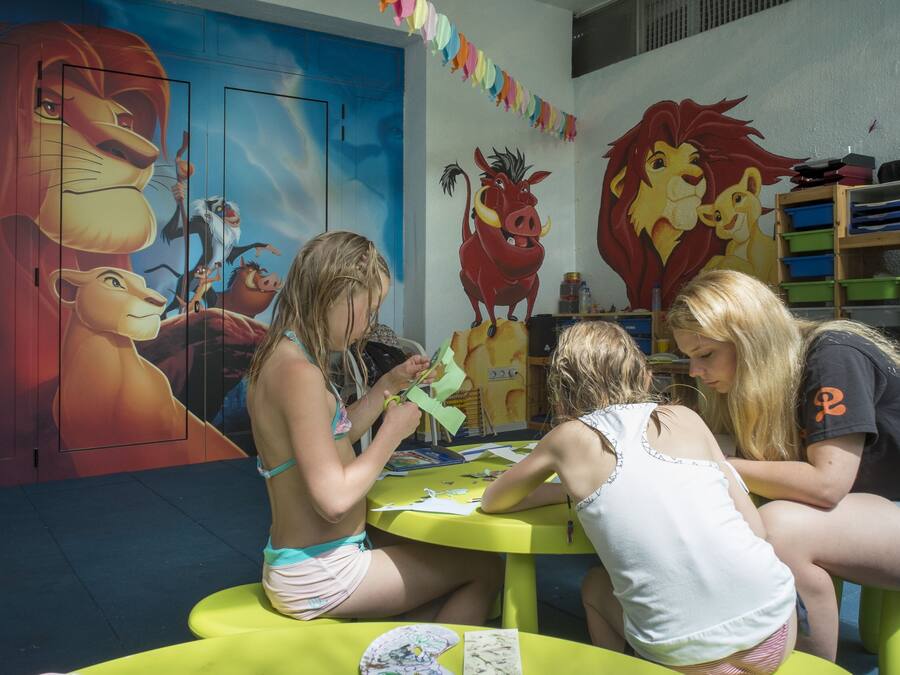 A room with a large mural of animated characters, a bright yellow table, and a bookshelf with various items.