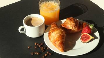 Un desayuno con un croissant, una fresa, un vaso de jugo de naranja y una taza de café sobre una mesa negra.
