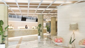 Un vestíbul ampli amb una recepció, plantes en testos i cadires de vimet.