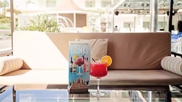 Un área de descanso con una mesa de vidrio, un sofá con cojines a rayas y un cartel que dice “HOTELINDALOPARK DRINKS” con diferentes bebidas.
