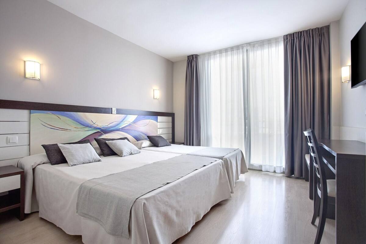 Una habitación de hotel con dos camas, un escritorio, un televisor de pantalla plana y un ventanal con cortinas.