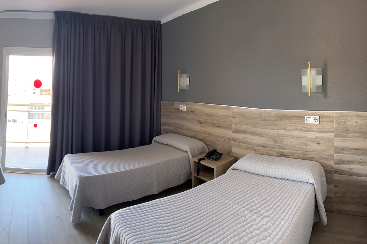 Une chambre d’hôtel avec deux lits, une tête de lit en bois, une table de chevet avec un téléphone et une vue sur l’extérieur.