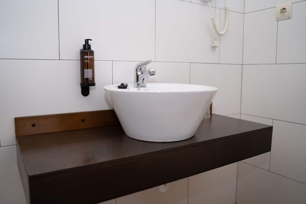 Une salle de bain avec un lavabo blanc, un plan de toilette foncé et un flacon de shampoing accroché au mur.