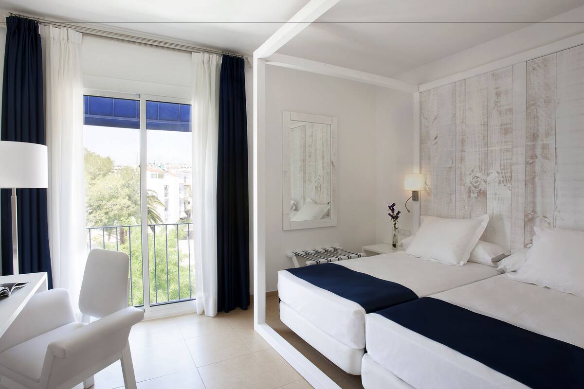 Une chambre d’hôtel avec un balcon, un bureau, deux lits et une vue sur la ville.