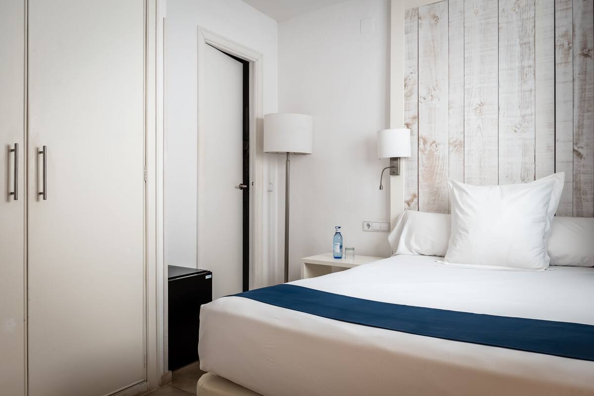 Une chambre d’hôtel avec un lit, une table de chevet, une lampe et une armoire.