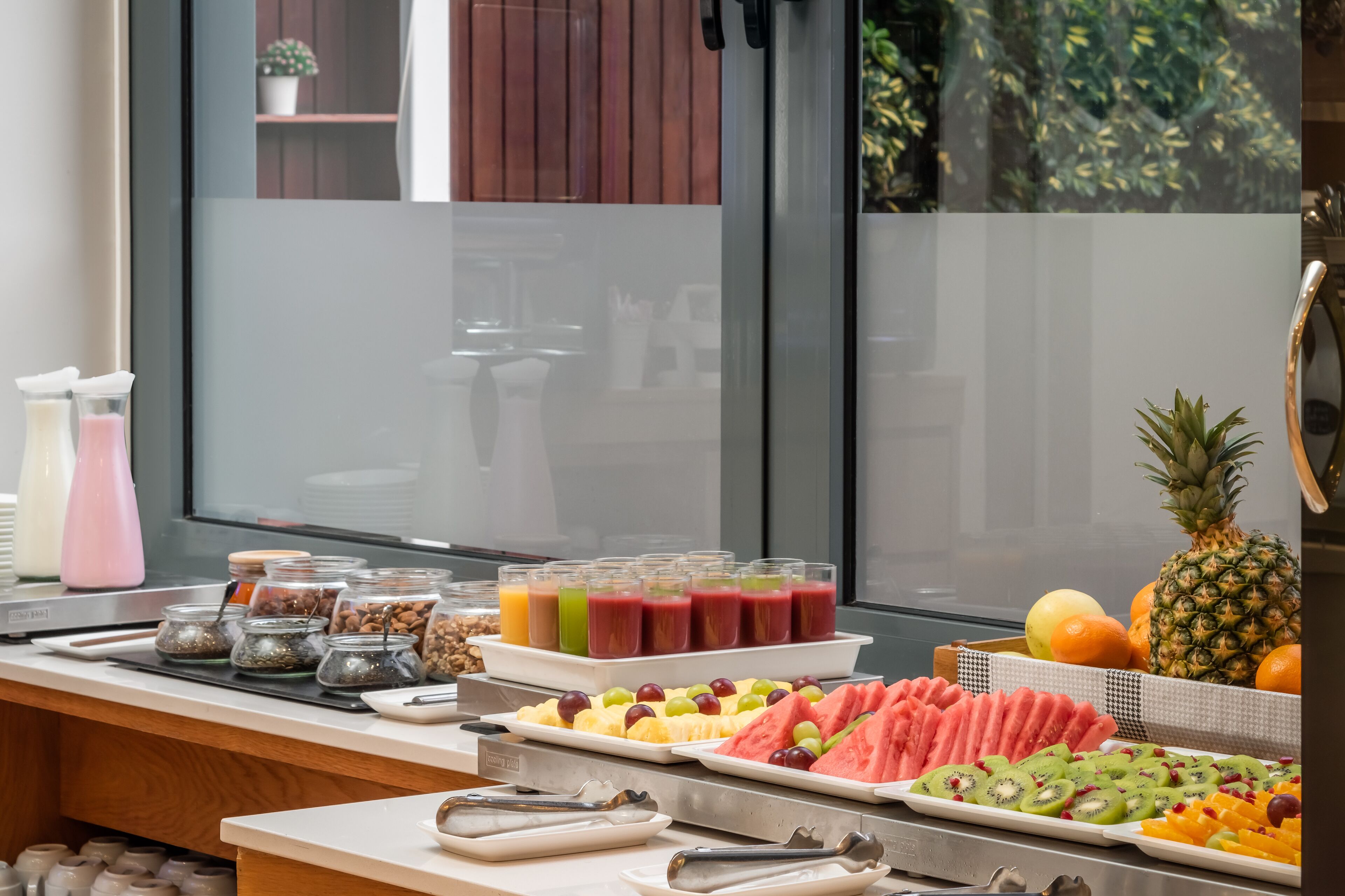 Un bufé de desayuno con diversas frutas, jugos y opciones de cereales.