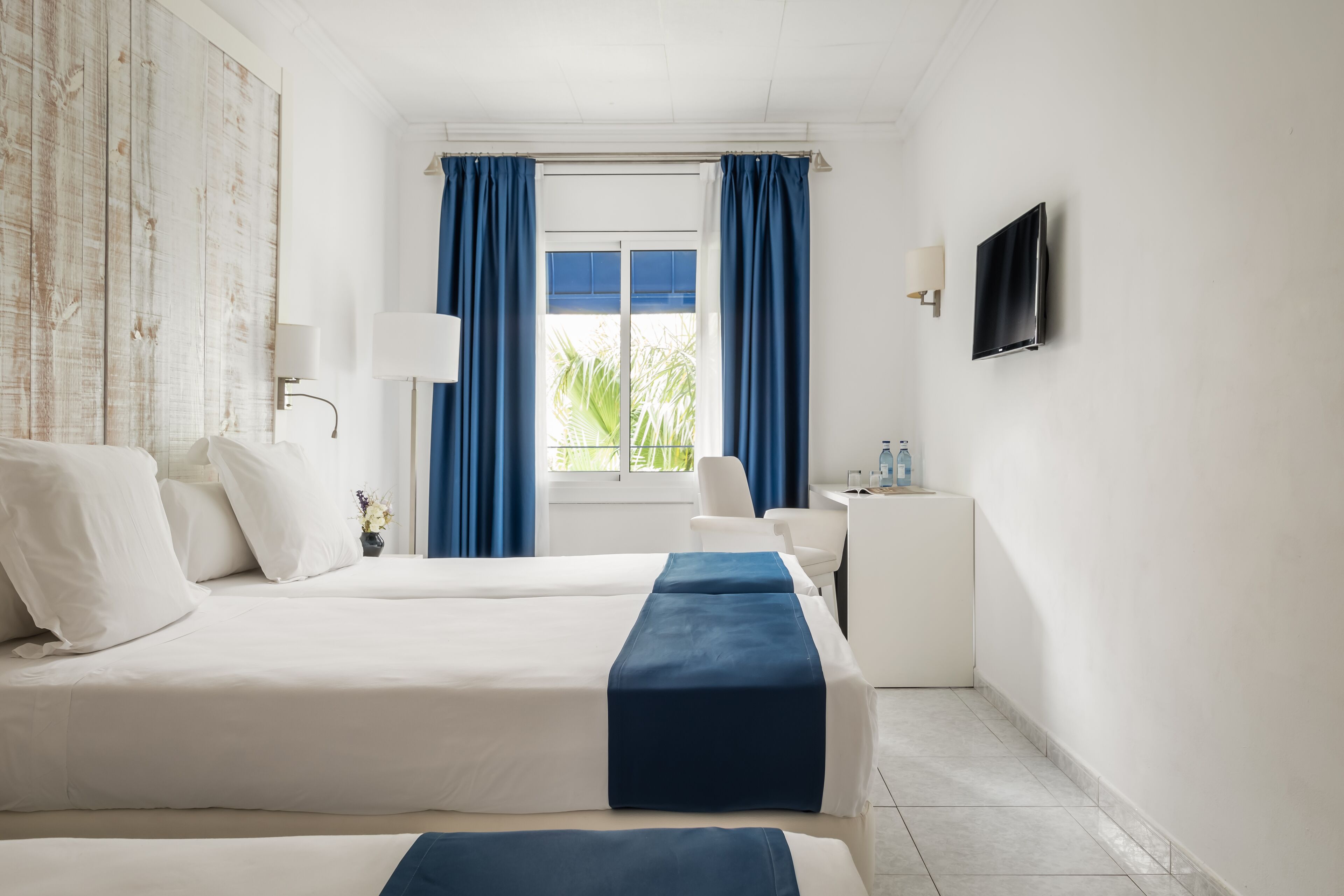 Een hotelkamer met twee bedden, een bureau, een televisie en een raam met gordijnen.