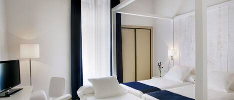 Habitación de hotel con dos camas, un escritorio con ordenador, una silla y televisión.