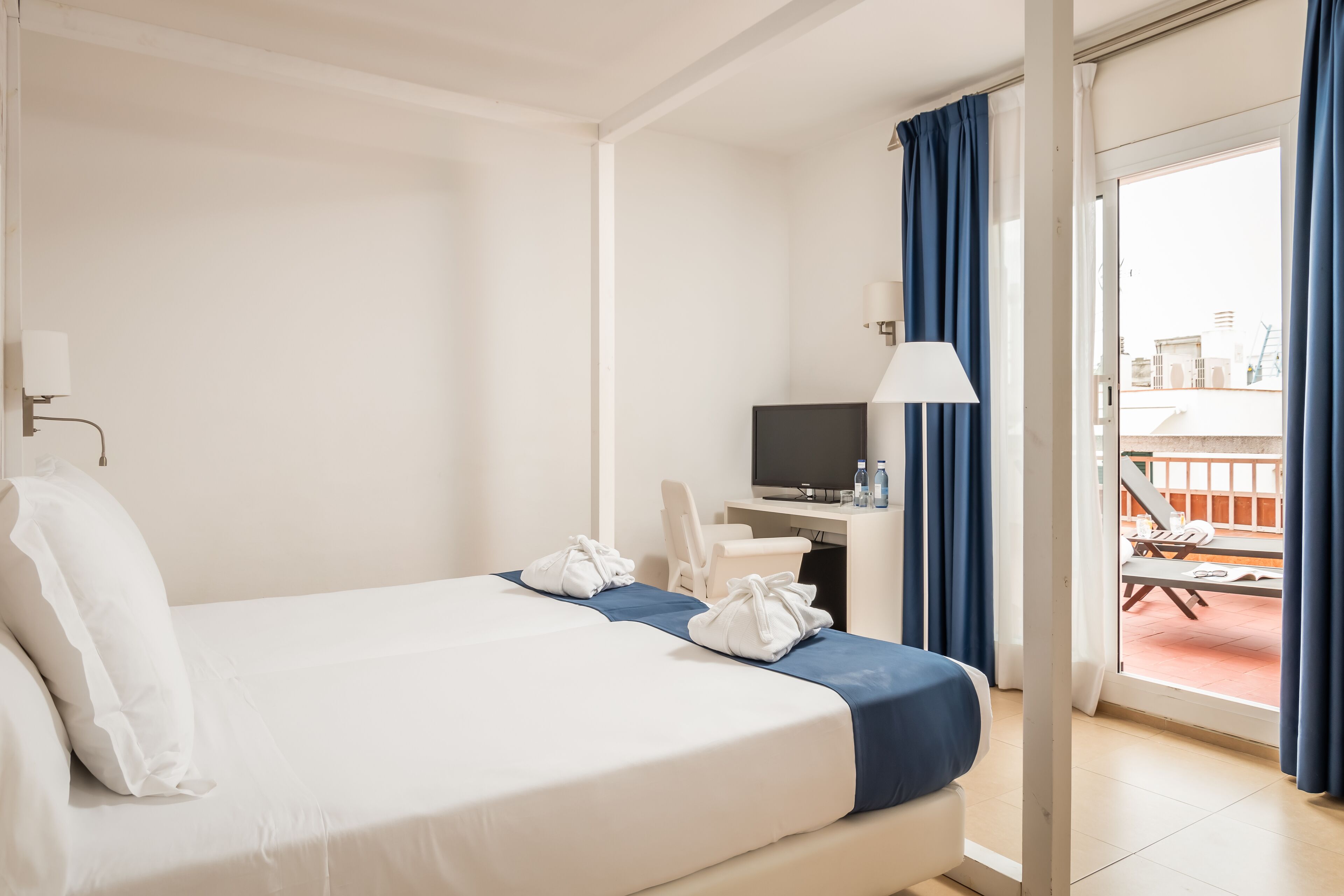 Ein Hotelzimmer mit Bett, Schreibtisch mit Fernseher, Stuhl und Balkon mit Tisch und Stühlen.
