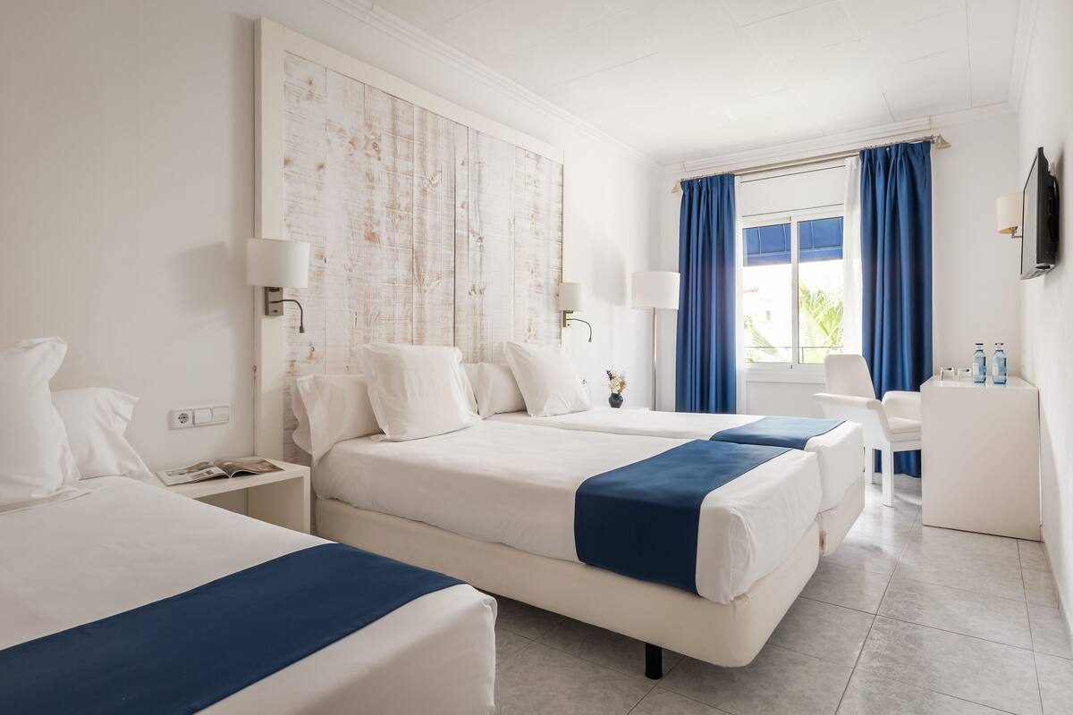 Une chambre d’hôtel avec deux lits, un bureau, une chaise et un téléviseur fixé au mur.