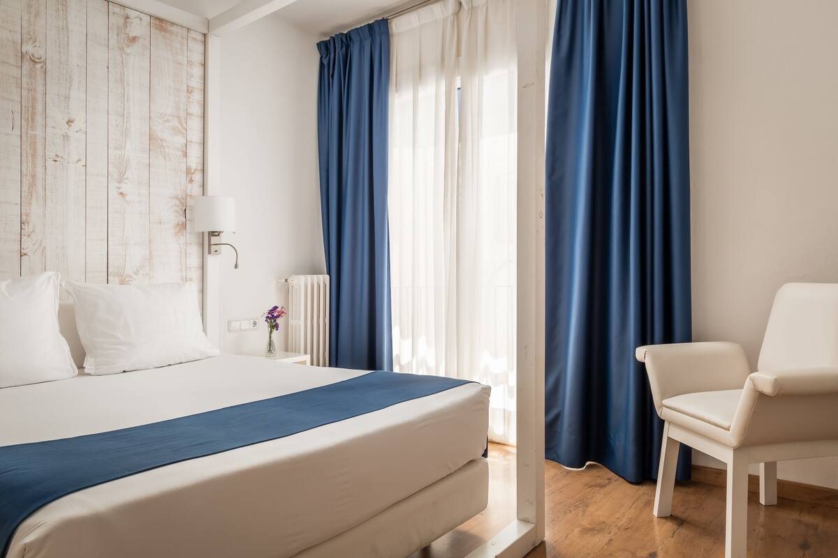 Une chambre d’hôtel avec un lit, une chaise, une lampe et des rideaux.