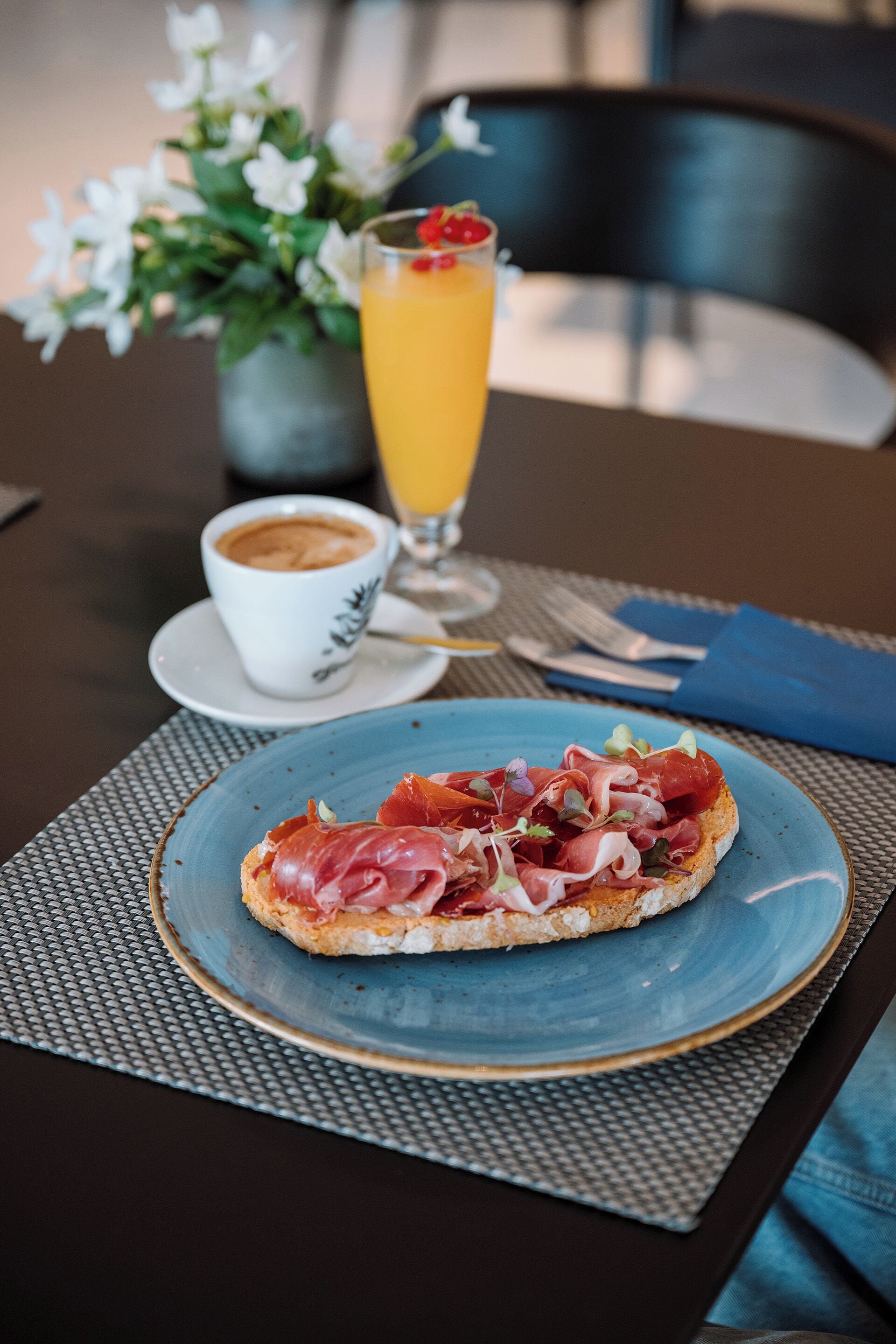 Une table avec une assiette bleue remplie de nourriture, une tasse de café et un verre de jus d’orange.