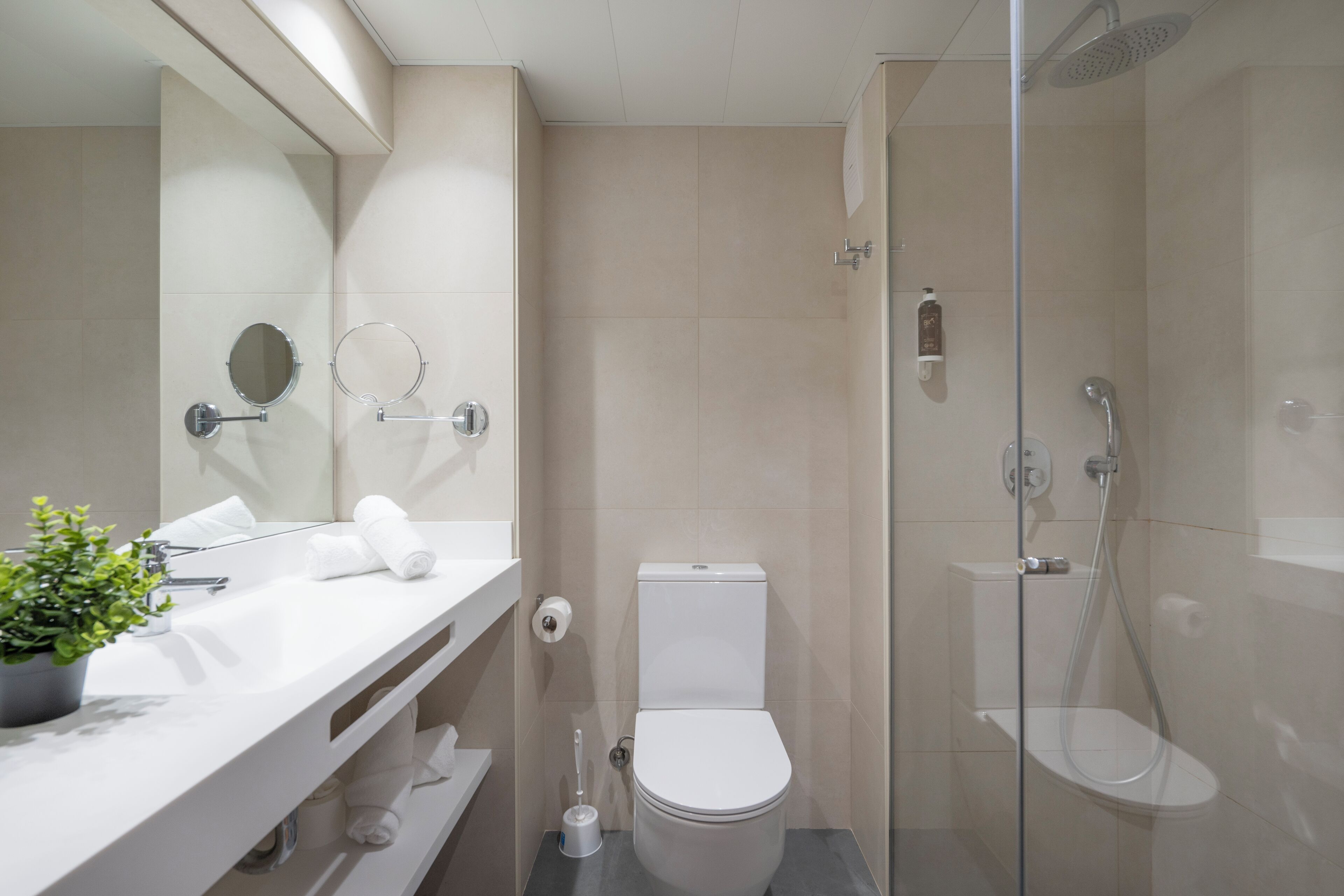 Un bany modern amb dutxa envidrada, un lavabo blanc amb mirall i un vàter.