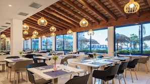 Ein Restaurant mit mehreren Tischen und Stühlen, großen Fenstern und hängenden Pendelleuchten.