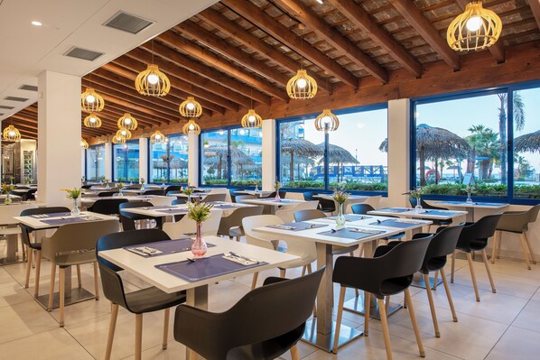 Un restaurant doté de nombreuses tables et chaises, de grandes fenêtres et de luminaires suspendus.