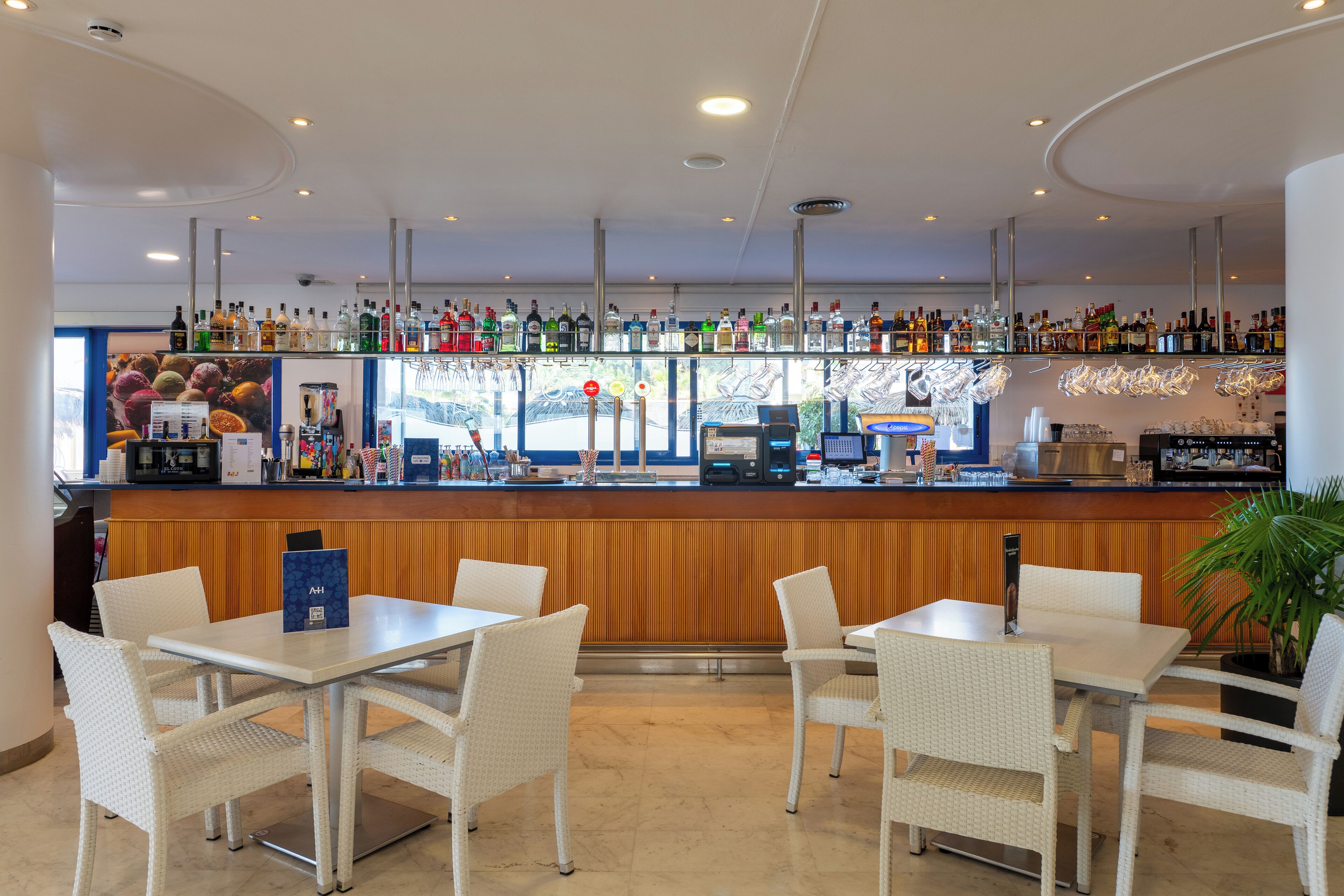 A bar area with multiple seating tables and chairs, a well-stocked bar counter with various bottles, and a wooden panel wall.