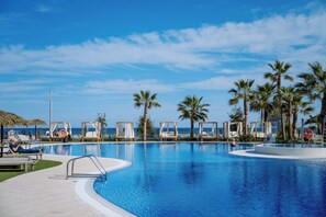 A pool area with lounge chairs and palm trees, overlooking a beach. - Hotel Tahiti Playa 4S (Santa Susanna)