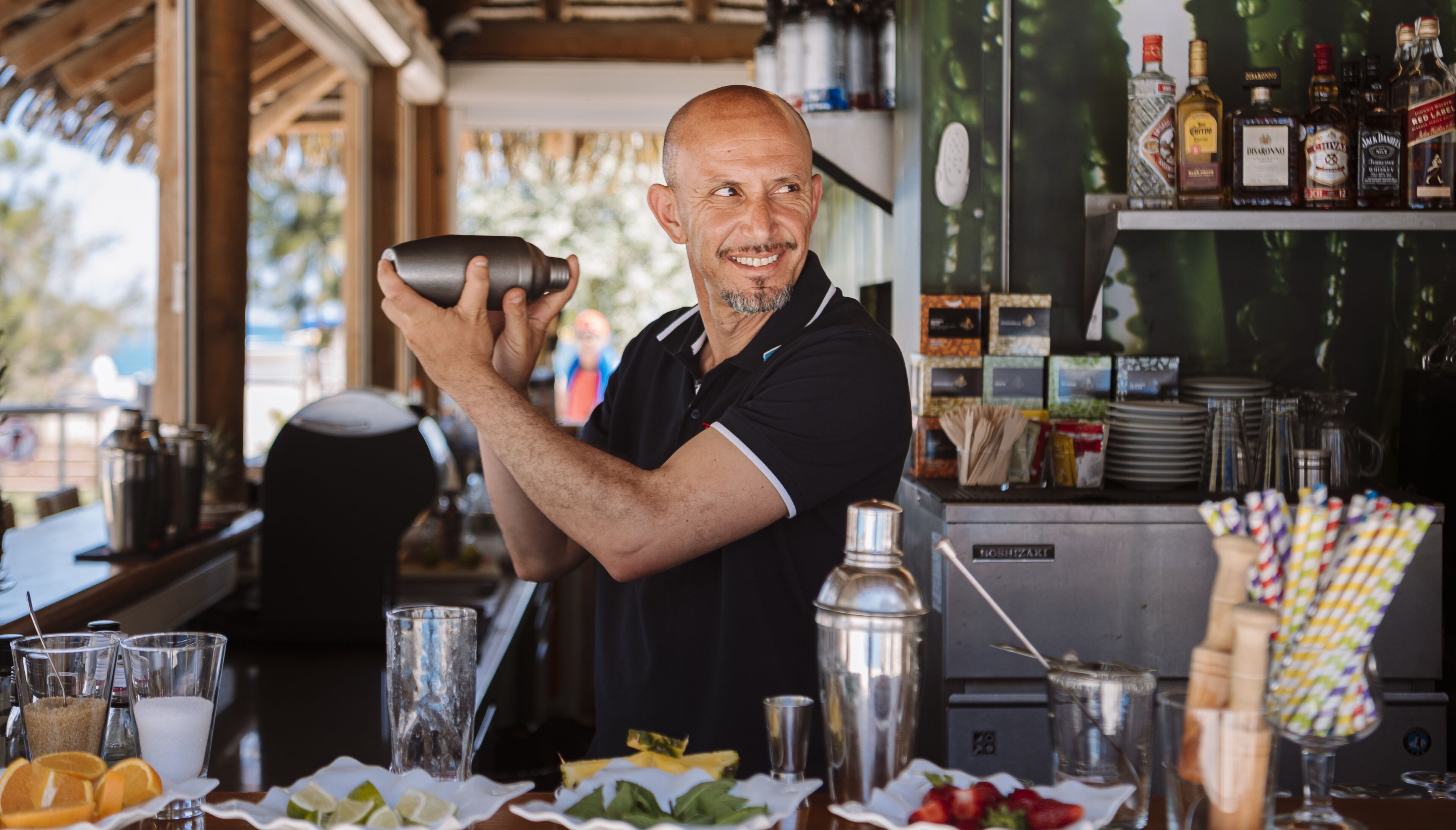 Un barman preparando una bebida en la barra, con varias botellas y vasos.