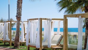 Eine Strandlounge mit Holzhütten, weißen Kissen und Blick auf das Meer.