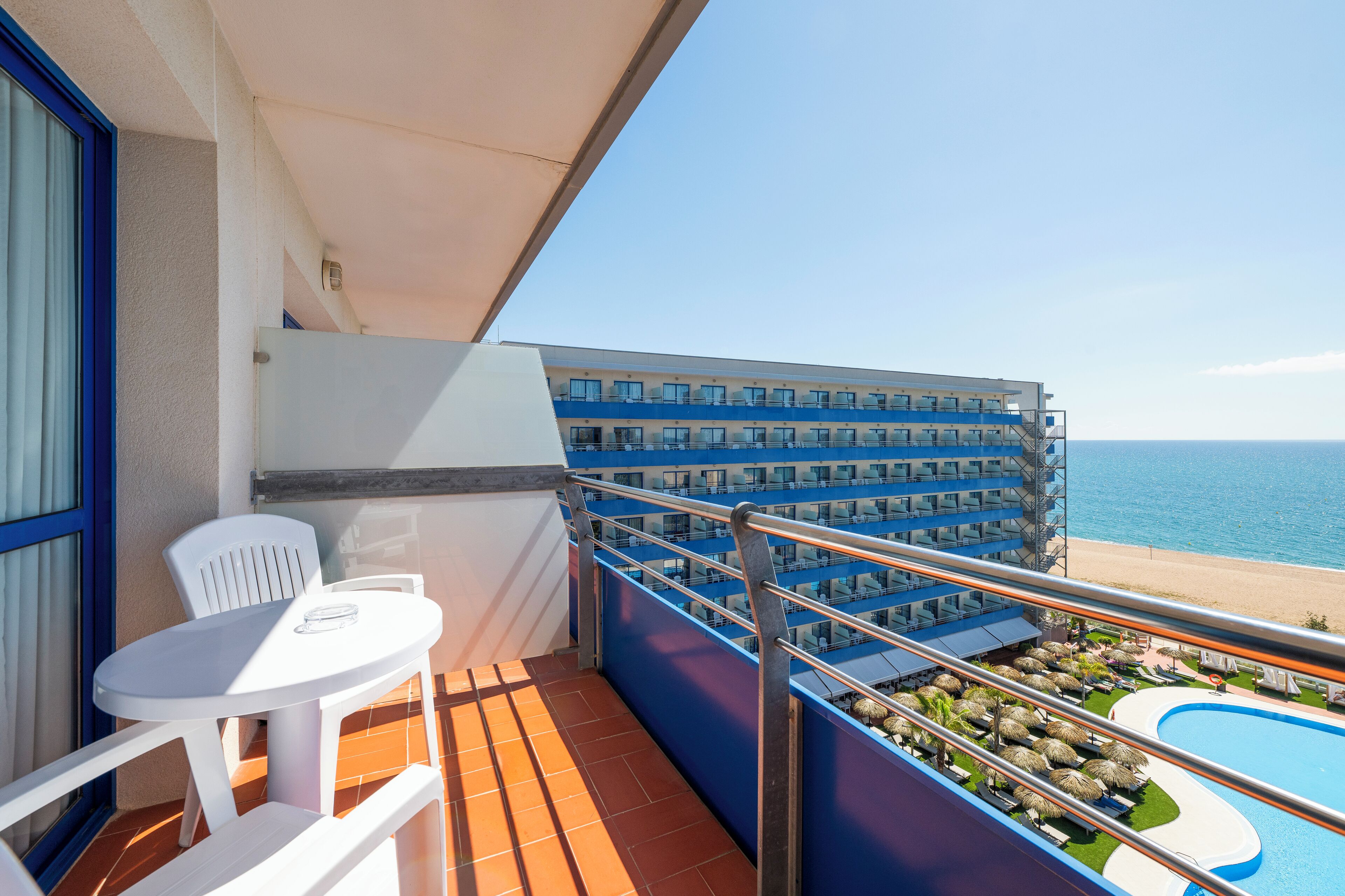 Ein Balkon mit weißem Tisch und Stühlen mit Blick auf Pool und Strand.