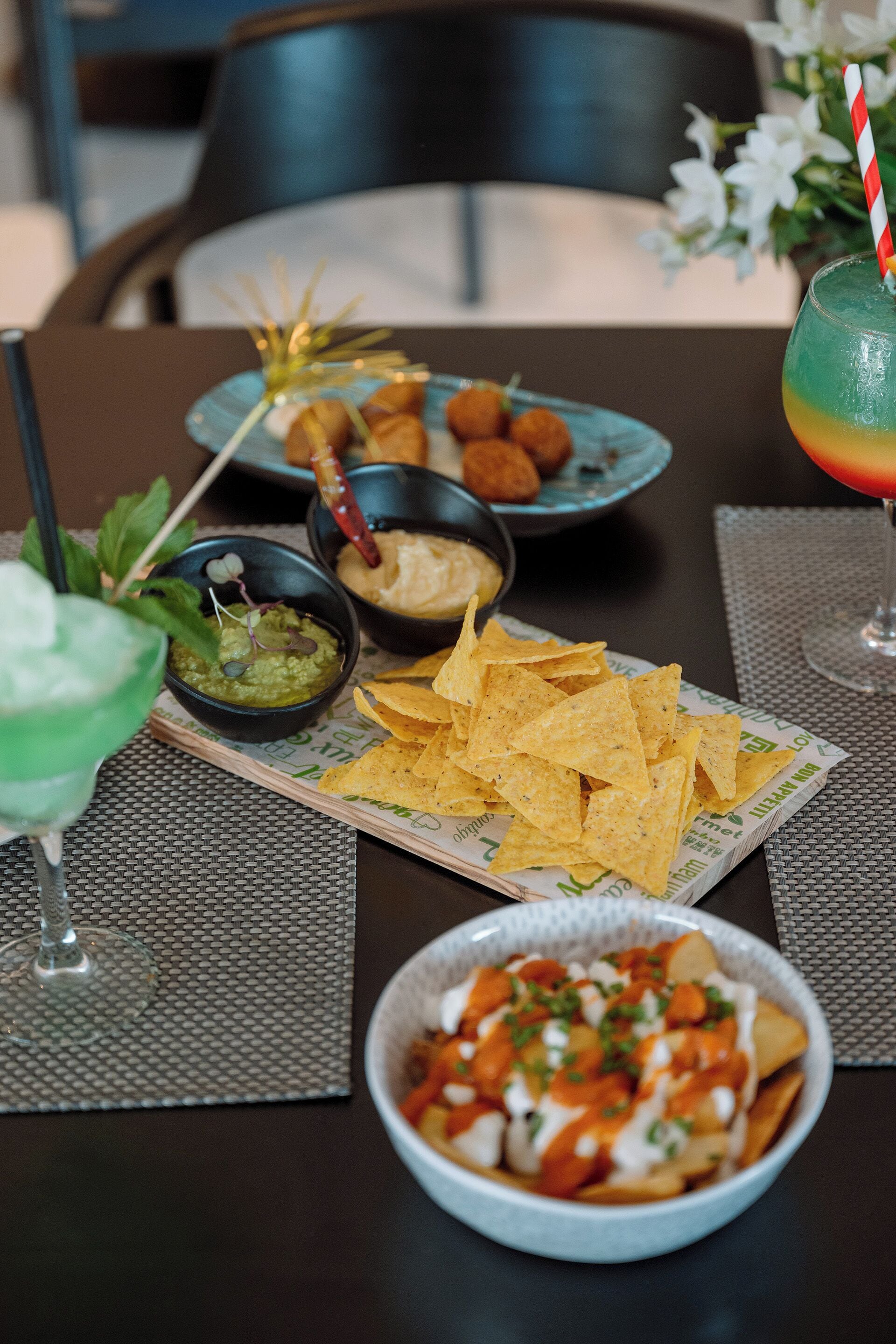 Una mesa servida con varios platos, entre ellos nachos, guacamole y una margarita.