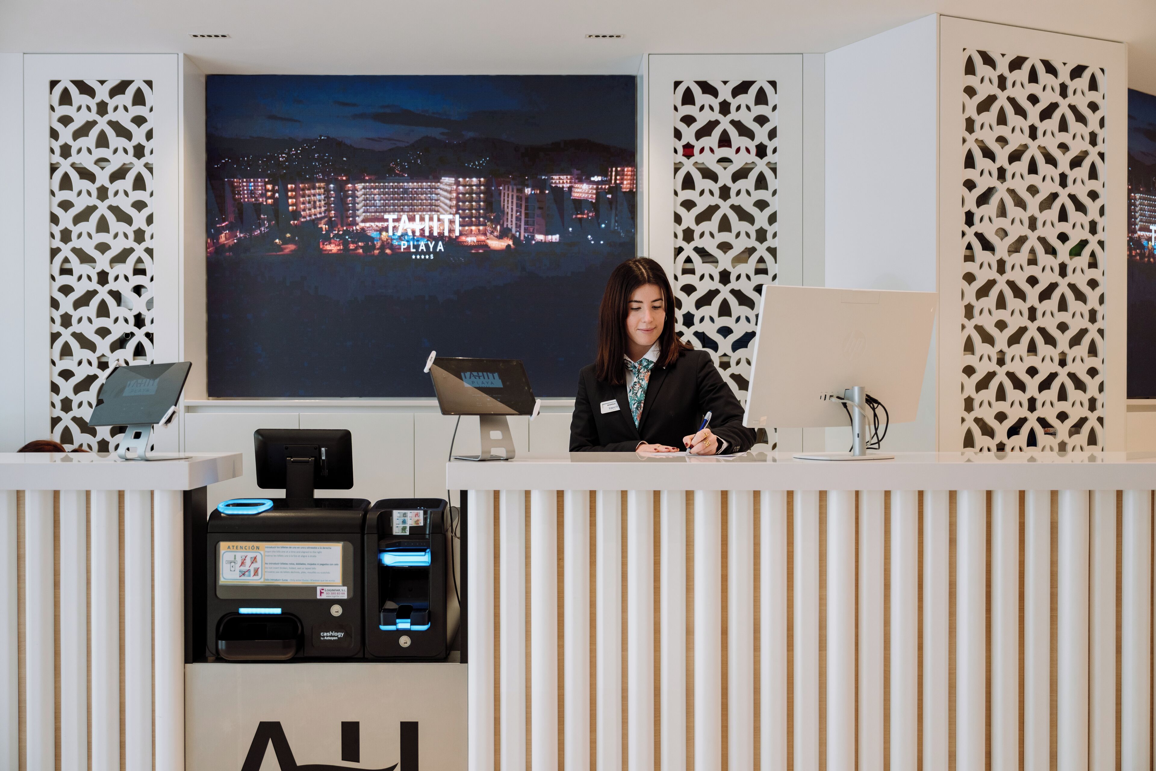 A reception desk with a cityscape view, a digital kiosk, and a name tag.