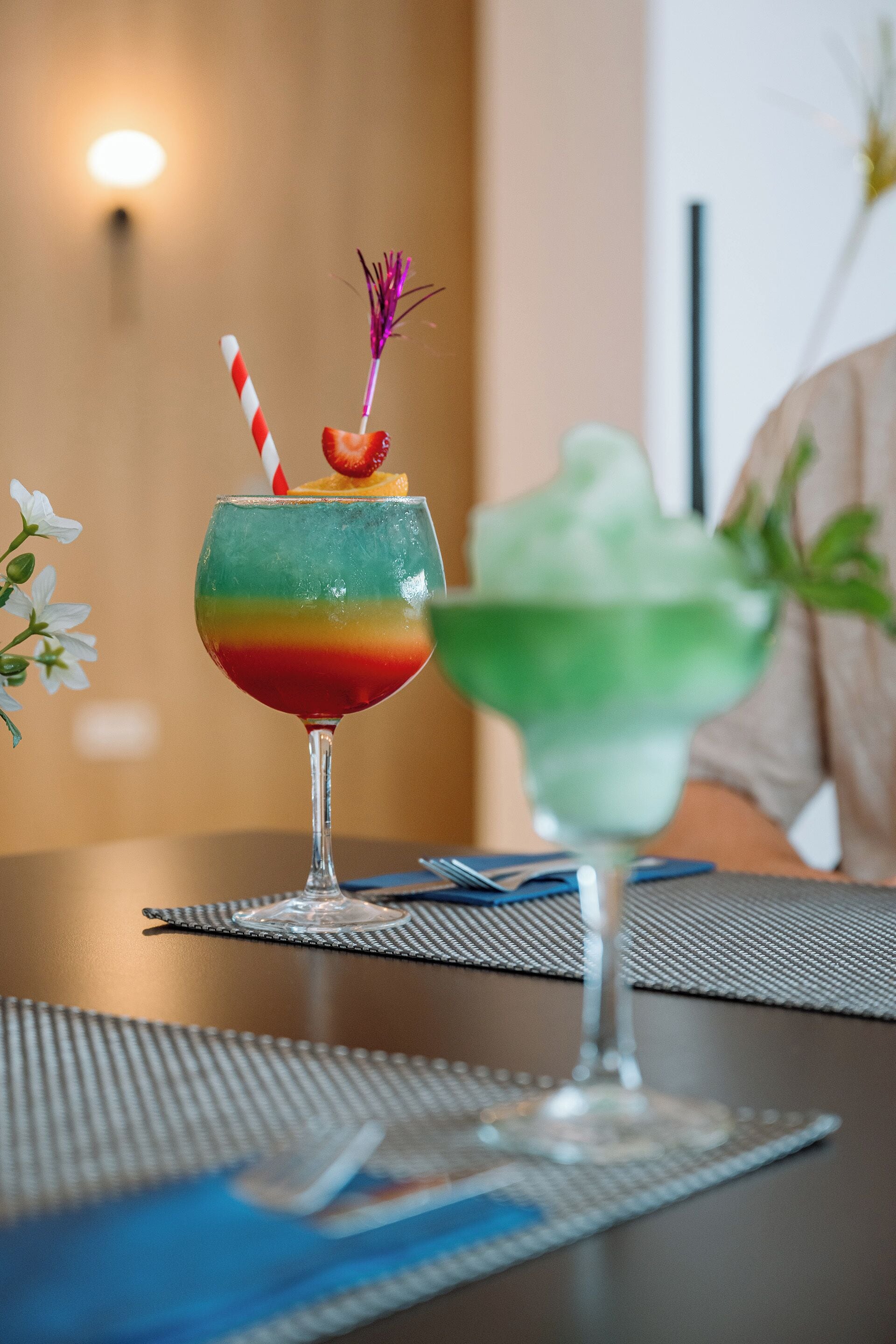 Two cocktails on a table with a striped placemat, a striped napkin, and a metal fork.