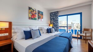 Ein Hotelzimmer mit zwei Betten, einem hölzernen Nachttisch, einem Sessel und einem großen Fenster mit Blick auf die Stadt.