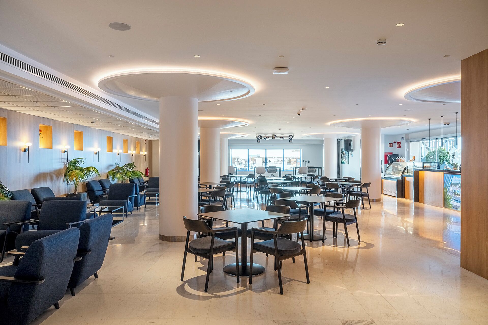 A spacious hotel lobby with multiple seating areas, a reception desk, and a view of the outside.