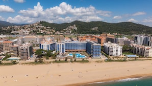 Ein Hotel an der Küste mit mehreren Gebäuden, einem Strand und einer Bergkulisse.