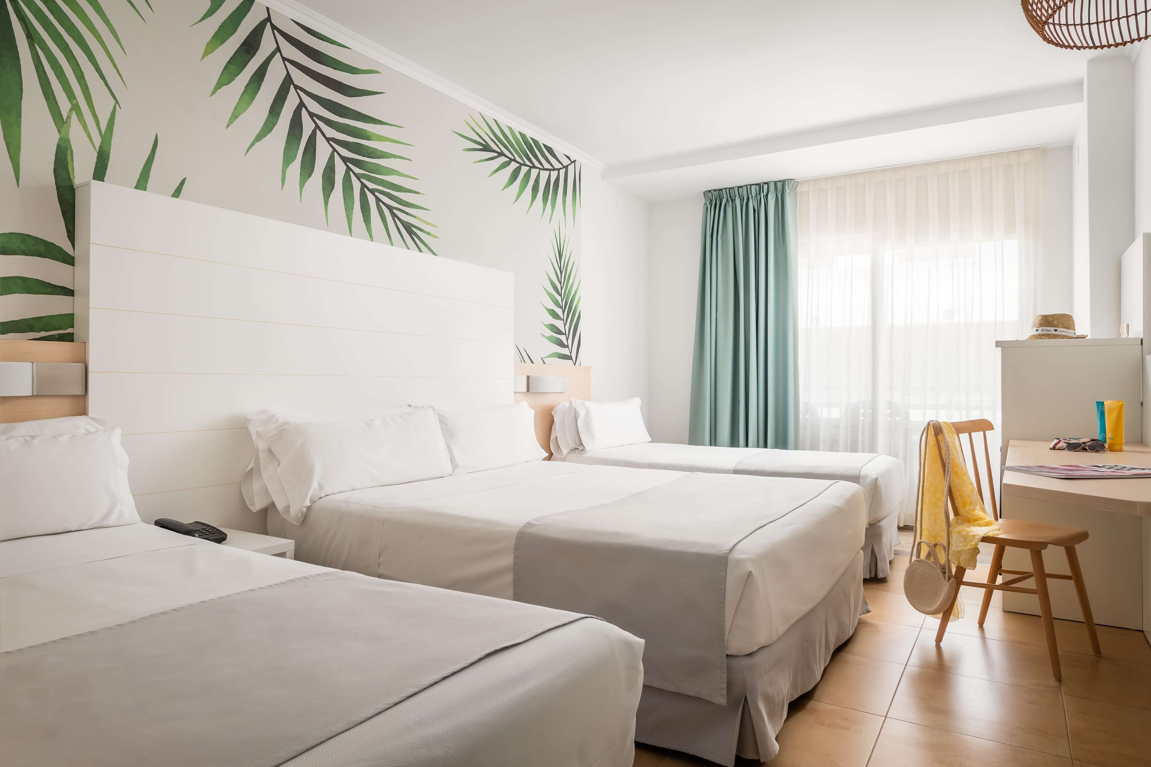 Habitación de hotel con dos camas, un escritorio, una silla, un teléfono y una ventana con cortinas.