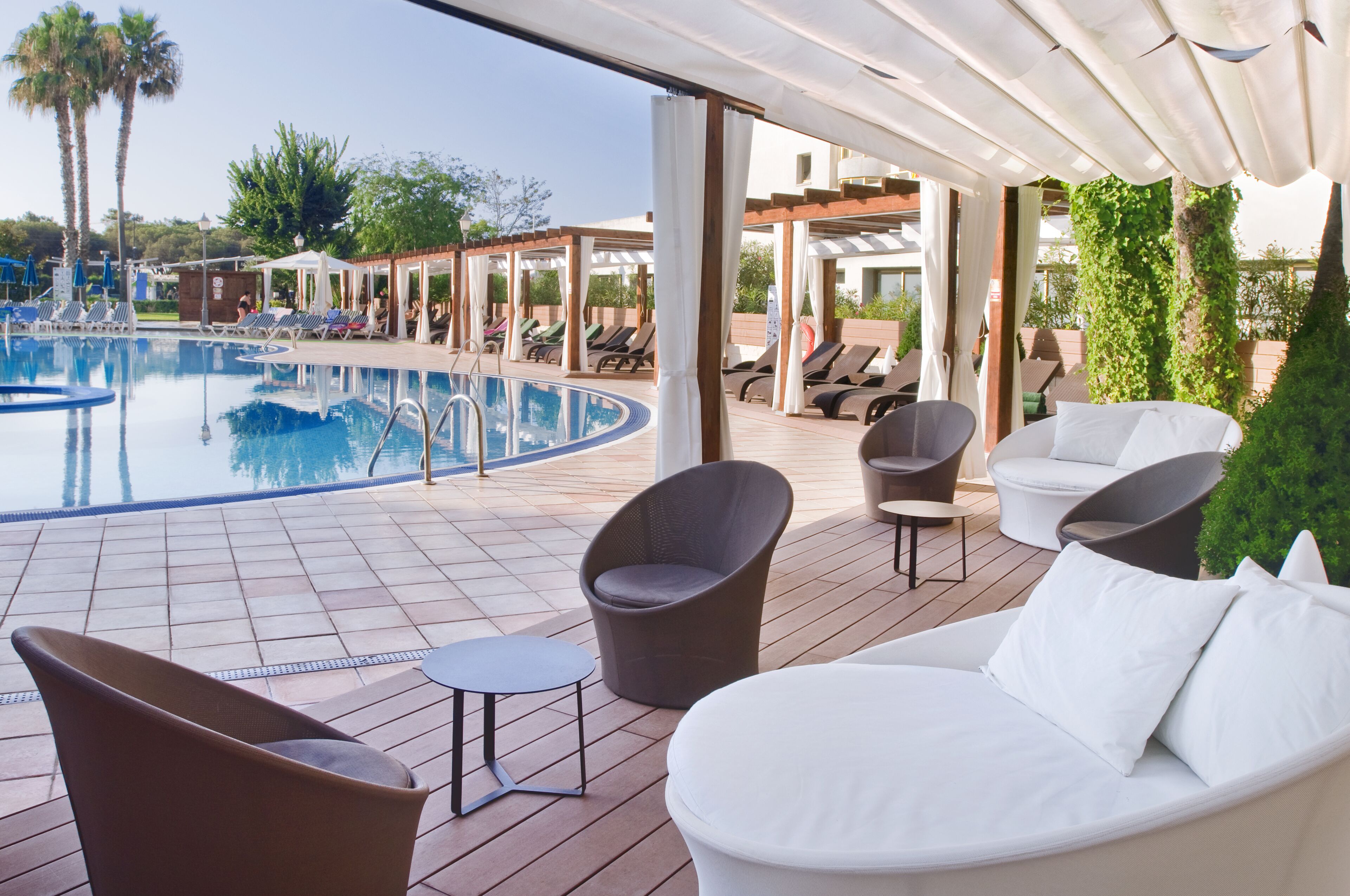 A poolside area with lounge chairs, a small table, and a covered seating area.