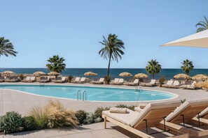 A poolside area with lounge chairs, palm trees, and a view of the ocean. - ME Sitges Terramar (Sitges)