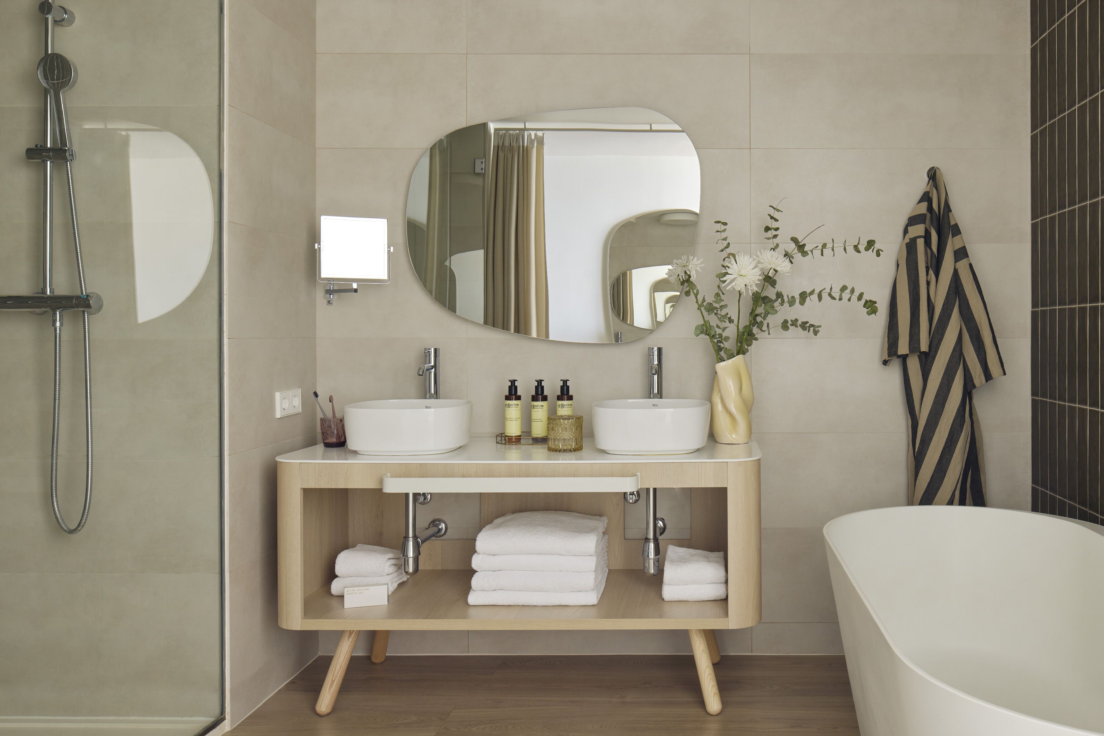 Et moderne badeværelse med et fritstående badekar, et toiletbord med to håndvaske, et stort spejl og en bruseniche.