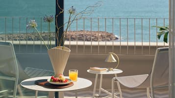 Un balcón con una mesa dispuesta para el desayuno, un jarrón con flores y vista al océano.