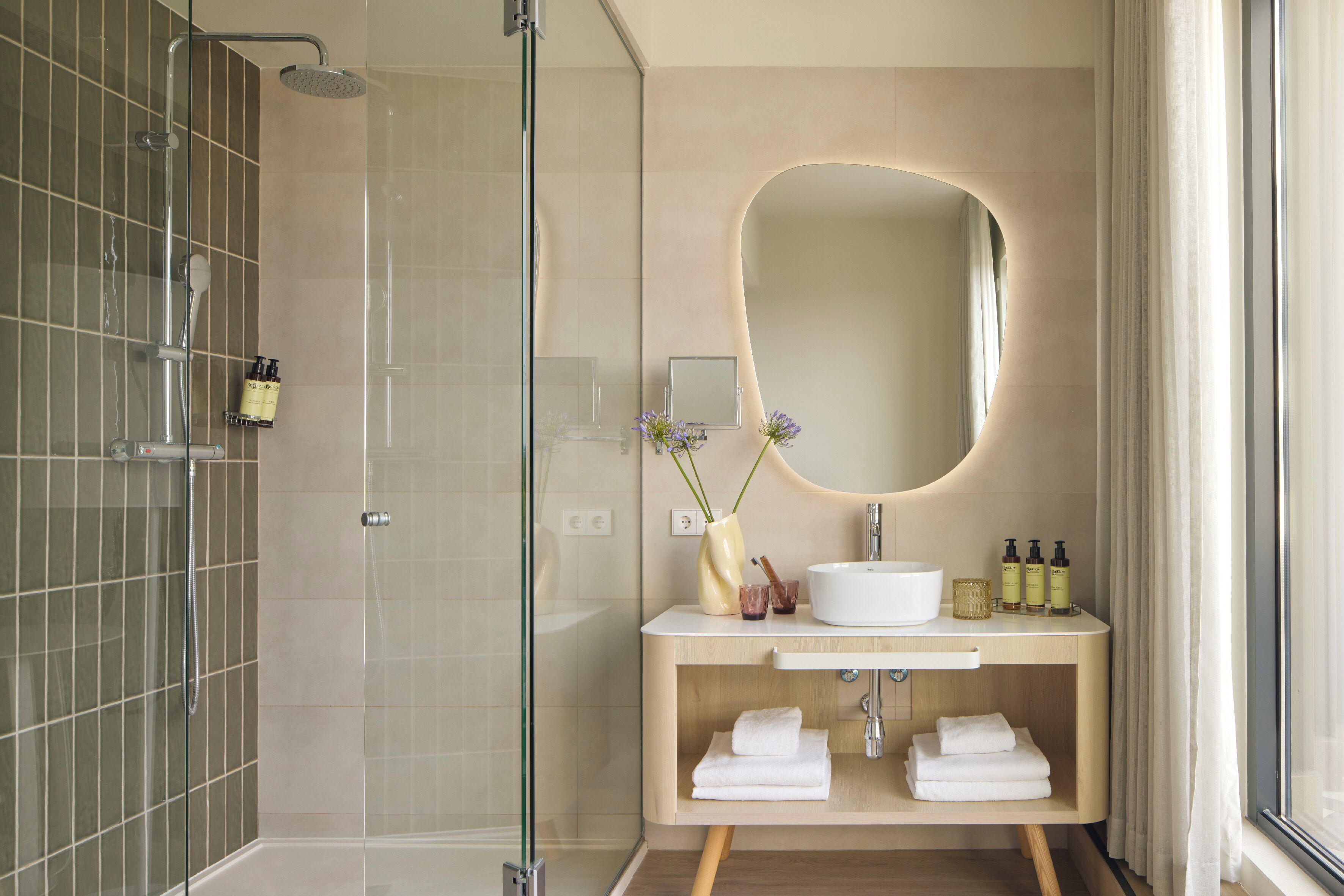 Un baño moderno con ducha envuelta en vidrio, tocador con lavamanos, espejo y espacio para toallas.