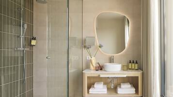 Un baño moderno con ducha envuelta en vidrio, tocador con lavamanos, espejo y espacio para toallas.