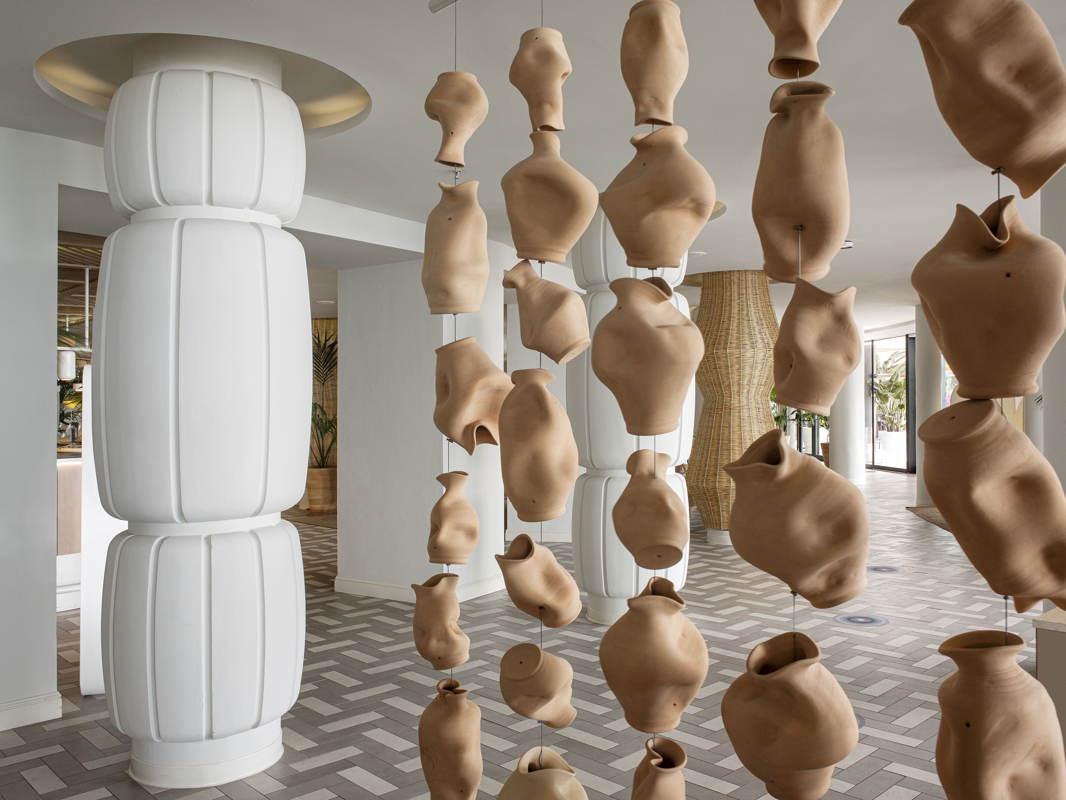 A modern interior with hanging pottery sculptures, white columns, and a herringbone floor pattern.
