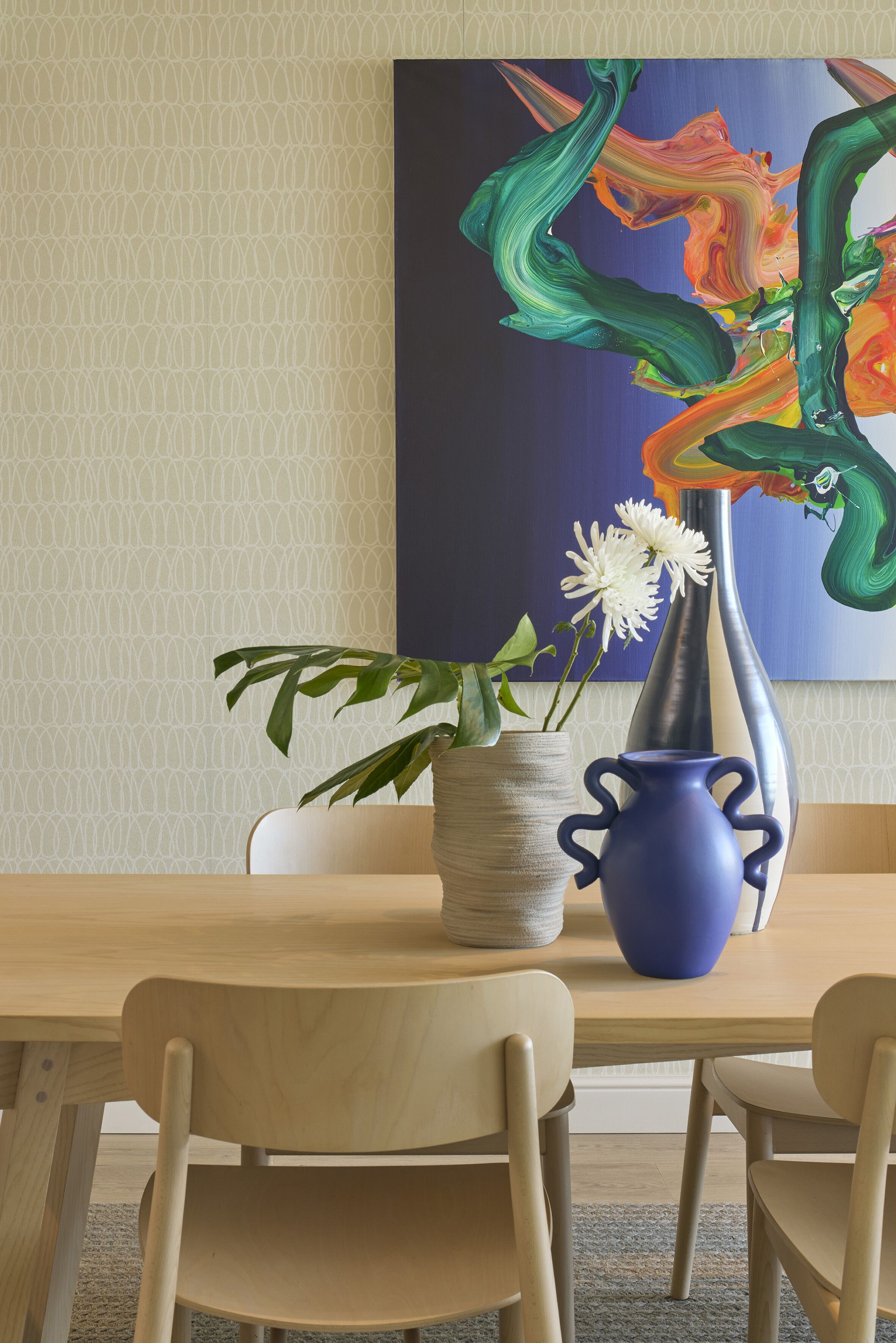 Une table à manger avec deux chaises, un vase bleu contenant des fleurs blanches et un vase texturé avec des feuilles vertes.